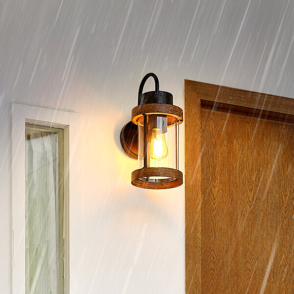 A Globe matte black outdoor wall sconce with faux wood accent and cylindrical glass shade on a wall outside.