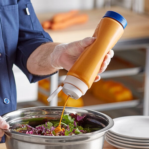 A hand using a Vollrath Traex squeeze dispenser with white cap to pour mustard into a bowl of salad.