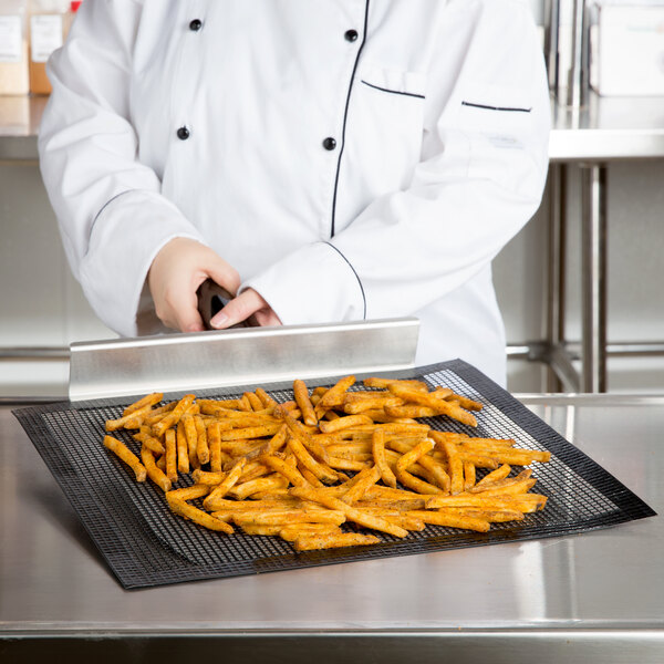 A person in a white coat uses an Essentialware mesh screen to cook french fries on a black tray.