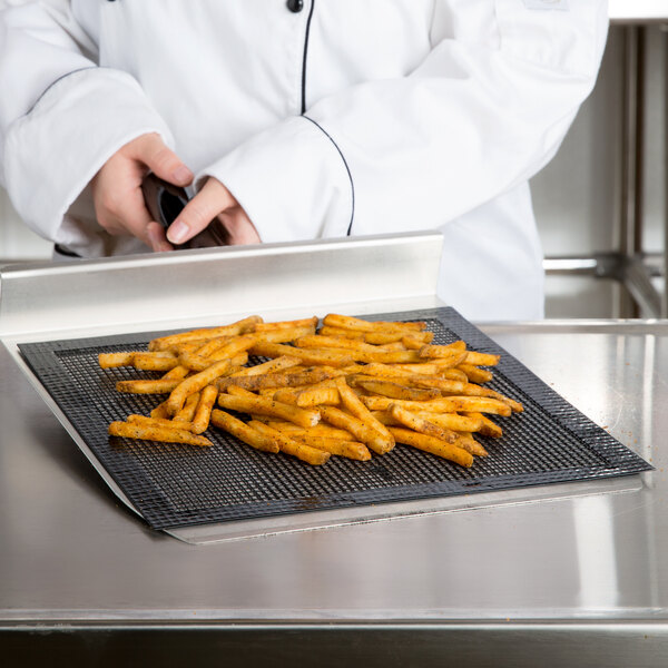 A person in a white chef's coat using an Essentialware loose weave mesh screen to cook french fries on a black grid.
