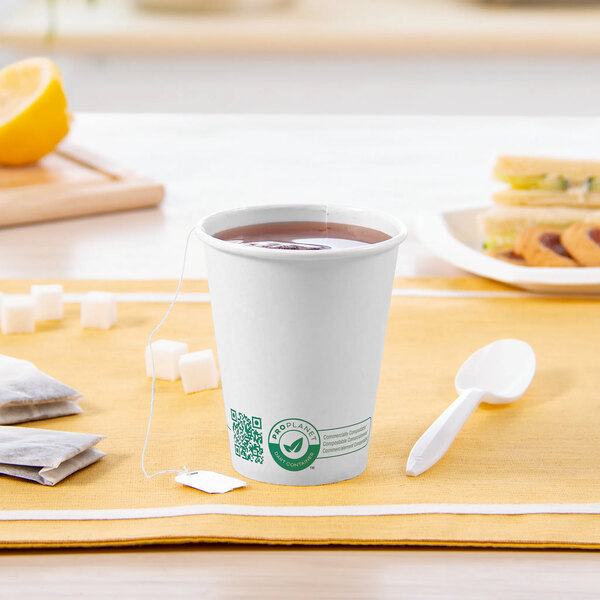 A Solo white compostable paper hot cup with brown liquid, a tea bag, and a spoon on a wooden surface.