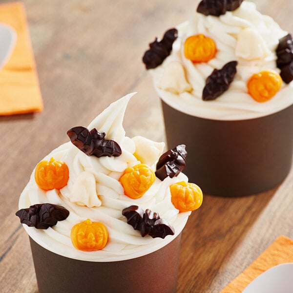 Two cupcakes with white frosting and orange and black decorations on a white plate.