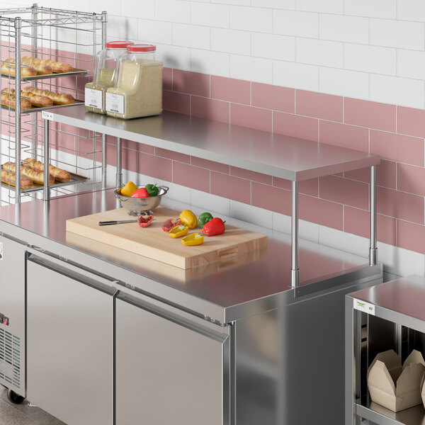 An Avantco stainless steel single deck overshelf on a counter in a kitchen with shelves of food.