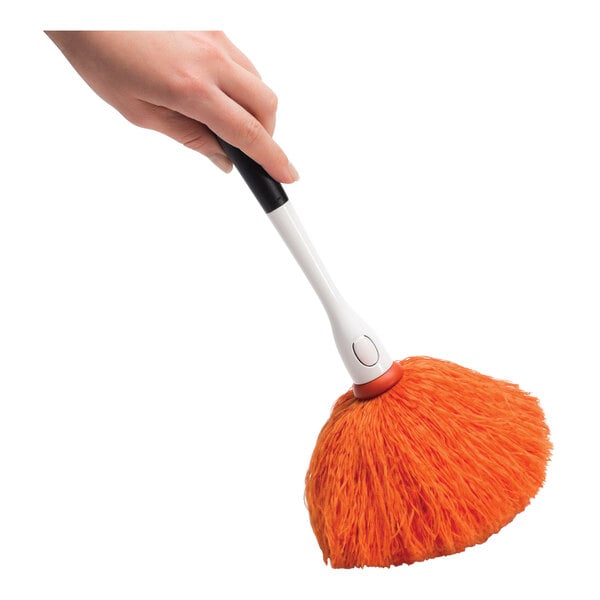 A handheld OXO Good Grips microfiber delicate duster with an orange cleaning head and a white handle.