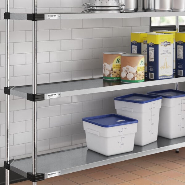 A metal shelving unit with solid shelves holding food containers and cans, set against a white tiled wall.