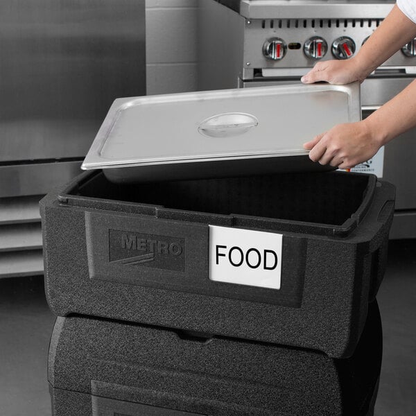 A woman using a Metro Mightylite BigBoy food pan carrier to hold a black food container.