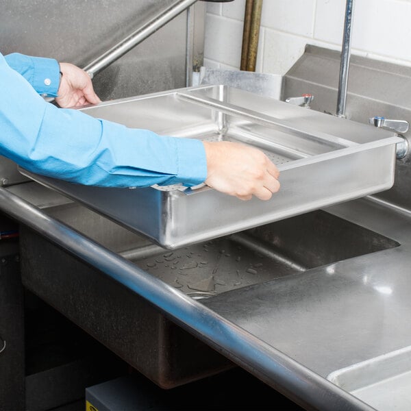 A person using an Advance Tabco pre-rinse basket over a sink.