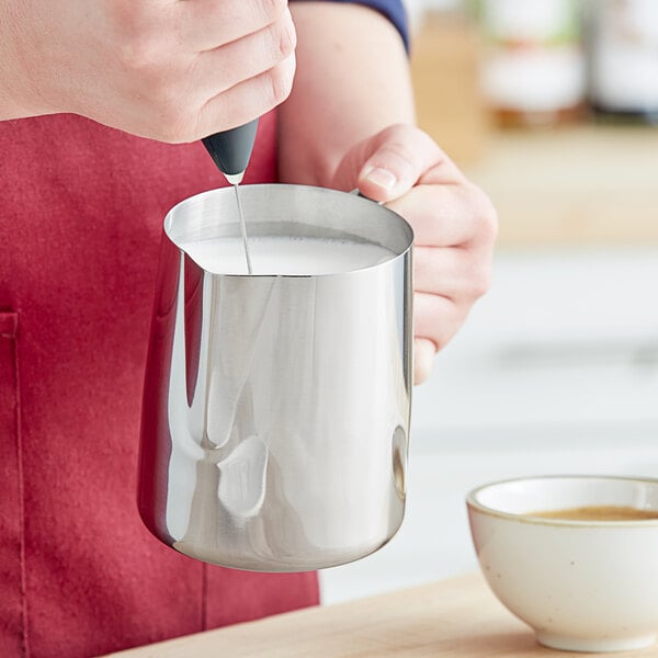 A person pouring milk into a Tablecraft stainless steel frothing pitcher.