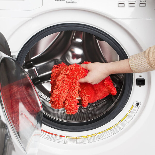 A person placing an orange microfiber duster refill into a front-loading washing machine.