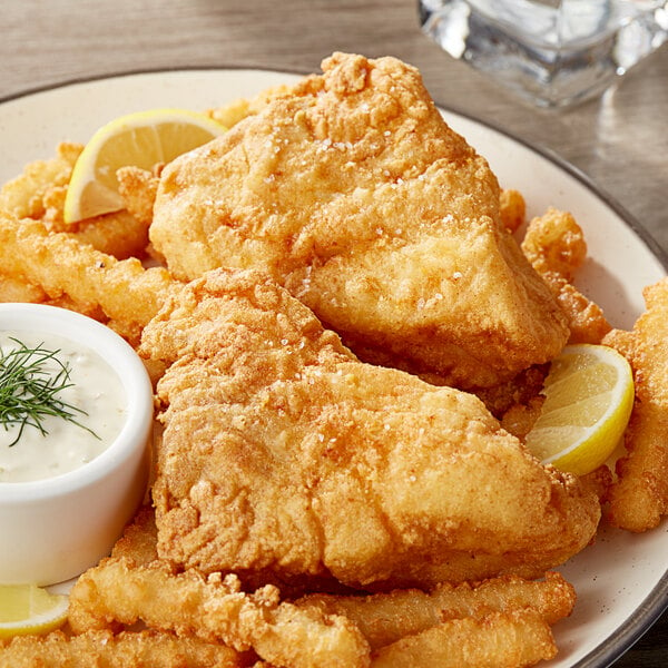 A plate of fried fish and fries with a lemon wedge and white sauce.