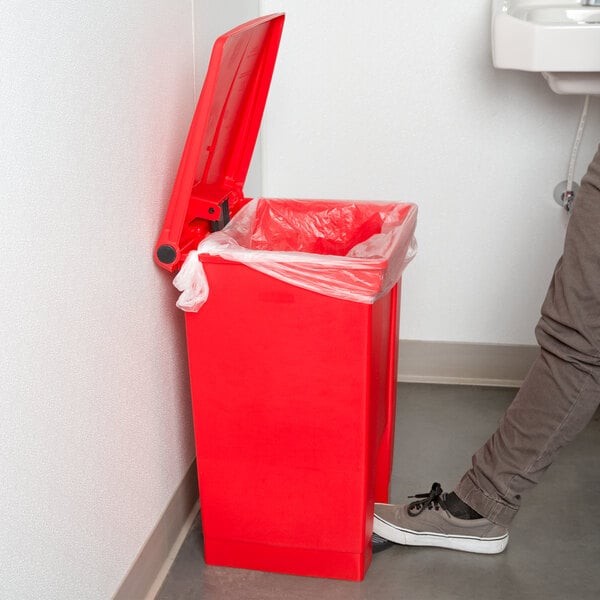 A person standing next to a red Rubbermaid step-on trash can.