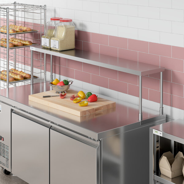 An Avantco stainless steel single deck overshelf on a counter in a kitchen with shelves of food.