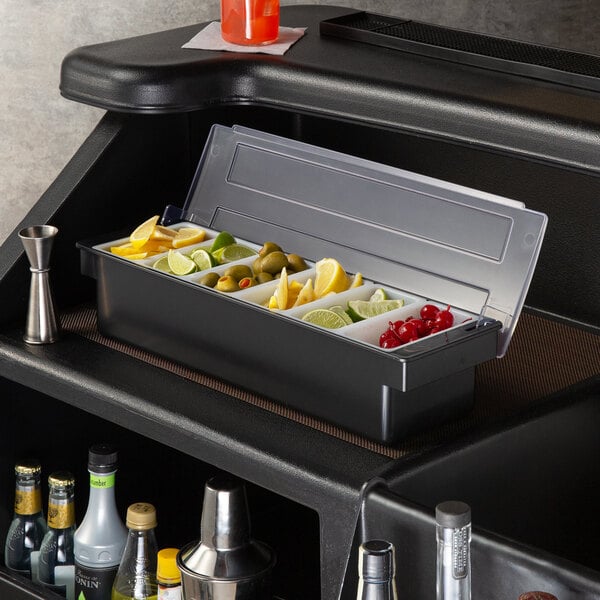 A Tablecraft 6-compartment condiment bar on a counter filled with fruit.