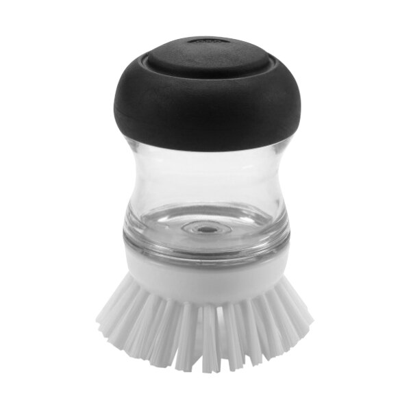 An OXO Good Grips white and black soap dispensing palm brush on a kitchen counter.