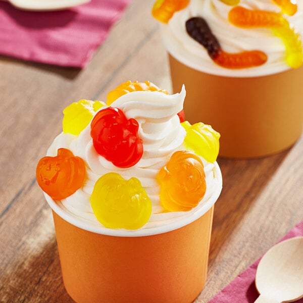 A close-up of a wooden spoon with Albanese Fall Gummi Pumpkins on top of a cup of ice cream.