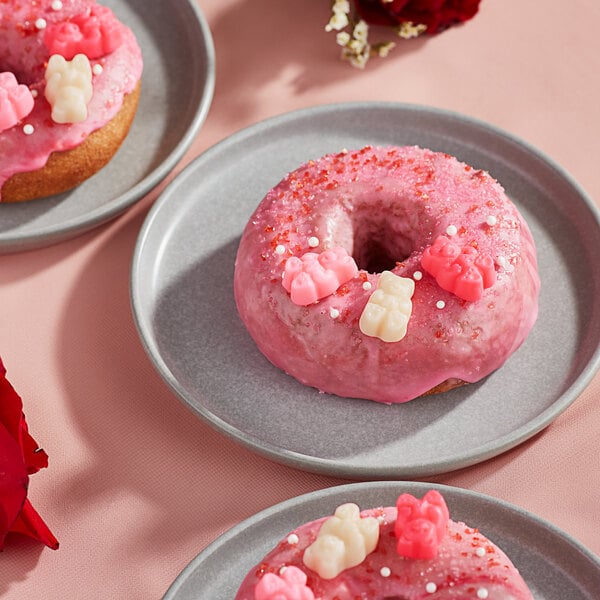 A close up of a pink doughnut with pink frosting and Albanese Lovestruck Gummi Bears on top.