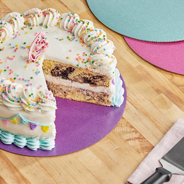 A Wilton corrugated glitter cake circle under a cake with a slice missing on a table.