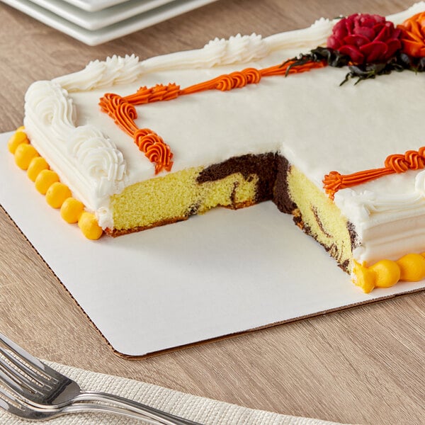 A Wilton white rectangular cake board under a cake with a slice missing.