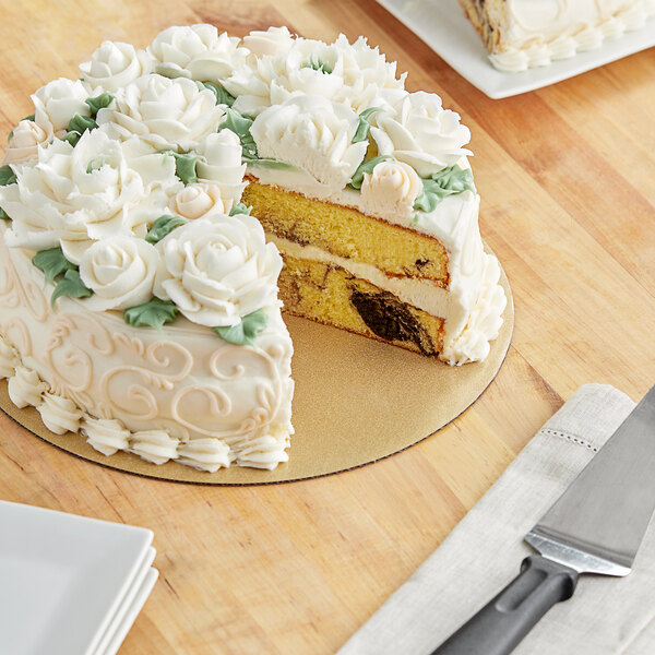 A cake on a Wilton gold glitter cake circle with white frosting and flowers on top.