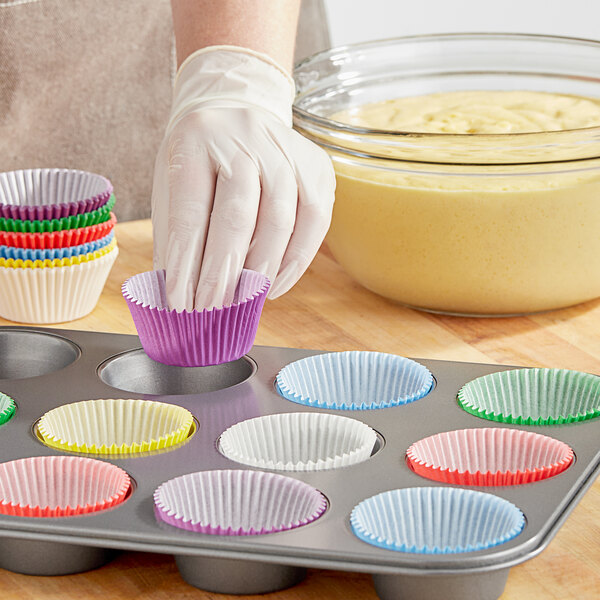 A person putting a Wilton assorted rainbow cupcake wrapper into a muffin tin.