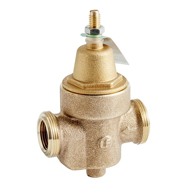 A close-up of a Watts brass water pressure reducing valve with a gold colored cap and a nut on a gold colored pipe.