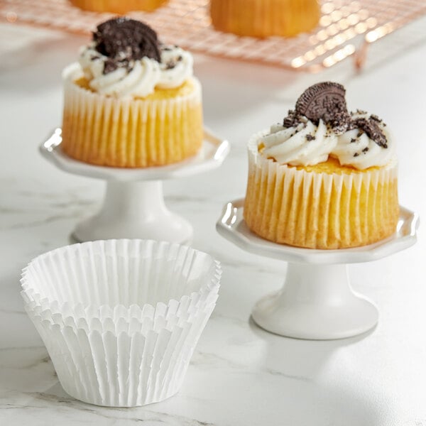 Two cupcakes with Wilton white jumbo baking cup wrappers on a white stand.