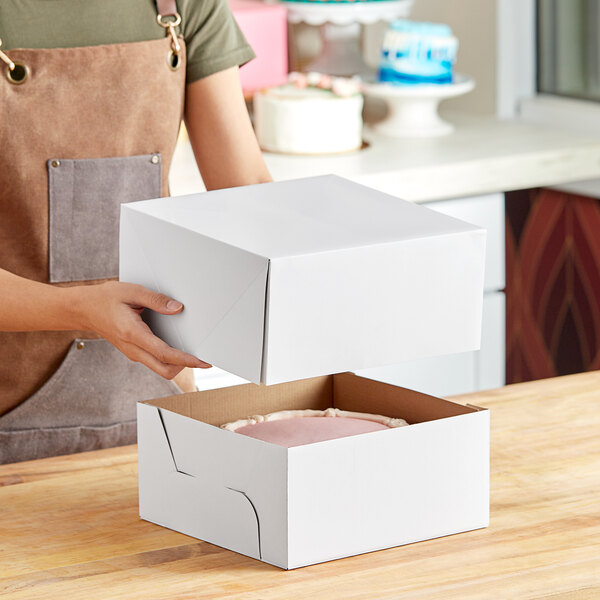 A woman holding a white Wilton cake box with a cake inside.