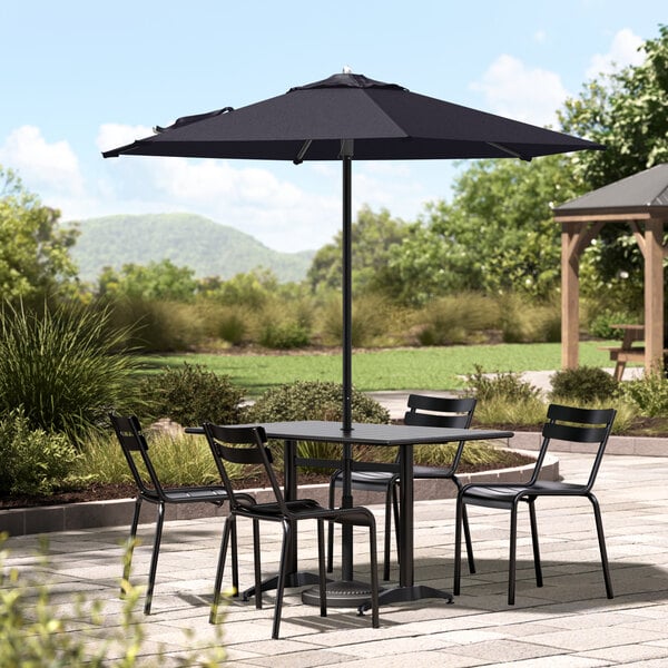 A table and chairs on a patio with a navy umbrella over it.