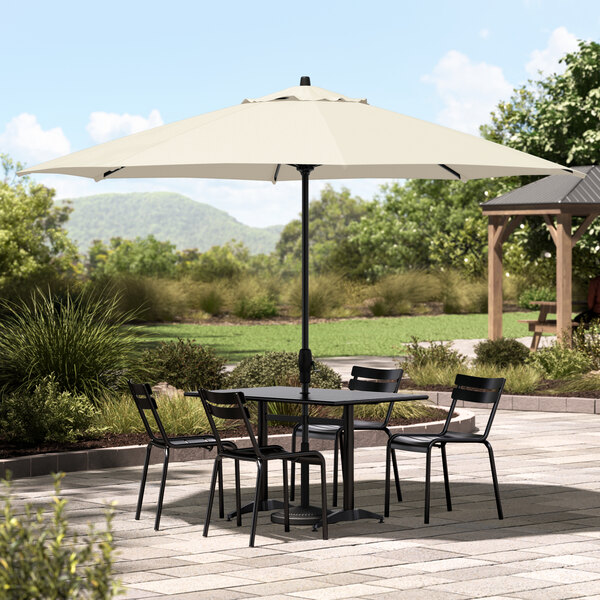 A table and chairs under a white Lancaster Table & Seating umbrella with a black pole.