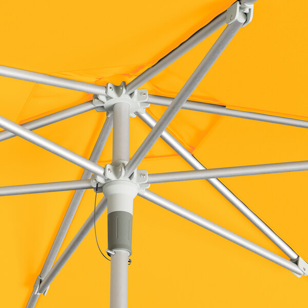 A close up of a Lancaster Table & Seating yellow umbrella with a silver aluminum pole and lift mechanism.