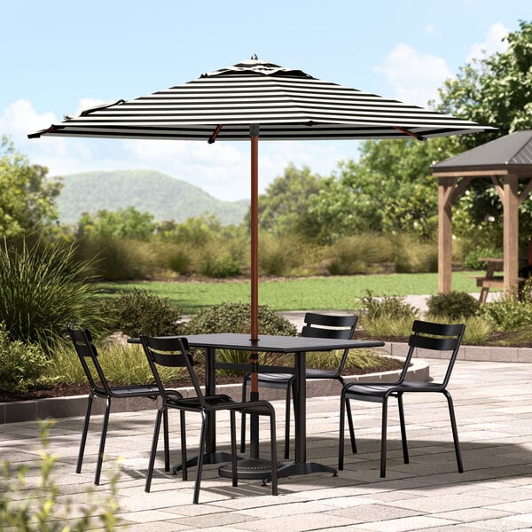 A Lancaster Table & Seating black and white striped umbrella on a patio table with chairs.