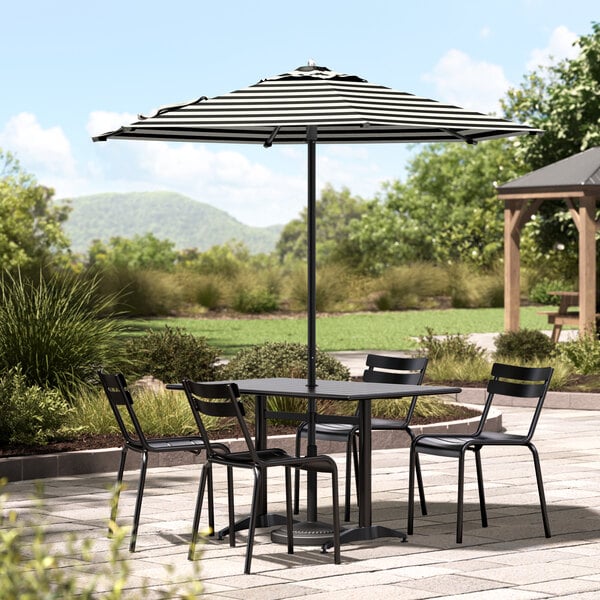 A black and white striped umbrella over a black table and chairs on a patio.