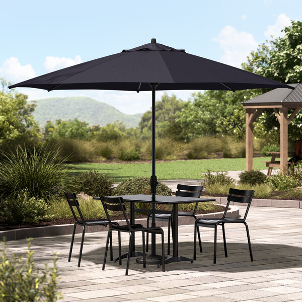 A table and chairs with a black Lancaster Table & Seating umbrella on a patio.