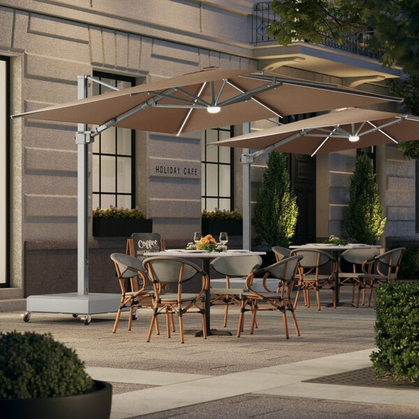 A Lancaster Table & Seating square wheat aluminum cantilever umbrella with lights on an outdoor patio table.