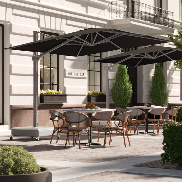 A black Lancaster Table & Seating cantilever umbrella over tables and chairs on a patio outside a restaurant.