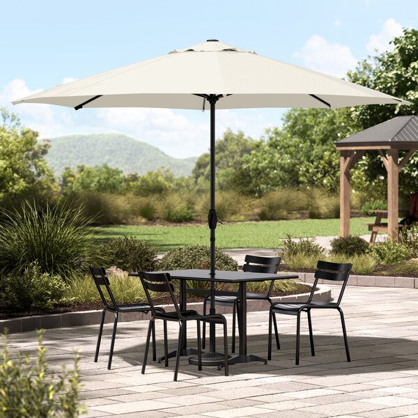 A white Lancaster Table & Seating umbrella over a table and chairs on an outdoor patio.