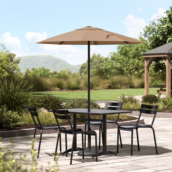 A table and chairs under a Lancaster Table & Seating black steel umbrella on a stone patio.