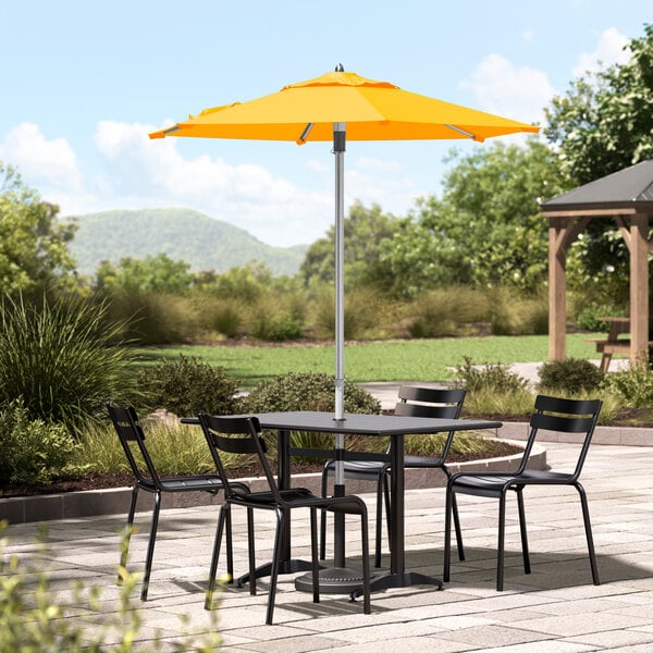 A Lancaster Table & Seating yellow umbrella over a table and chairs on a stone patio.