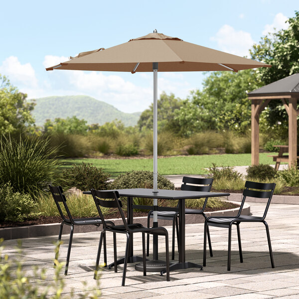 A Lancaster Table & Seating umbrella shading a table and chairs on a stone patio.