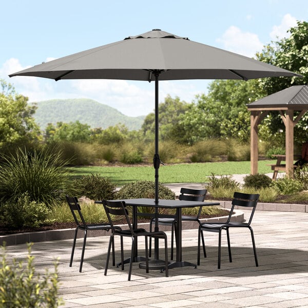 A Lancaster Table & Seating black steel umbrella over a table and chairs.