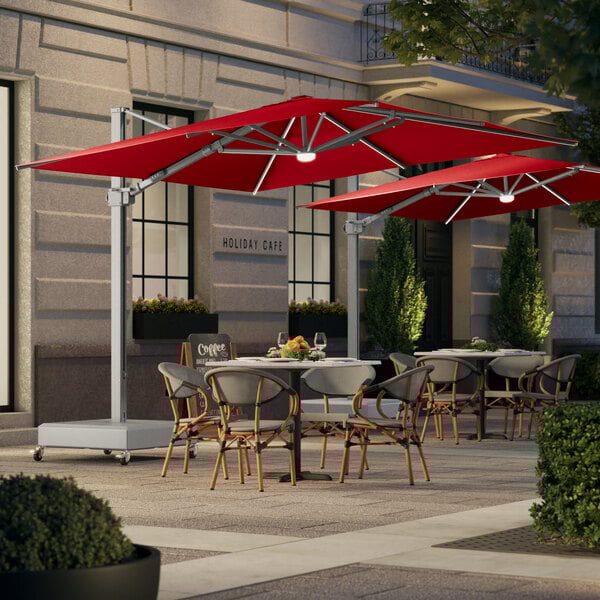 A red Lancaster Table & Seating cantilever umbrella with lights over a table on a patio.