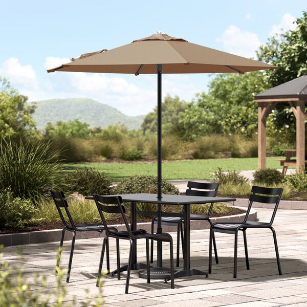 A Lancaster Table and Chairs under a black umbrella on a patio.