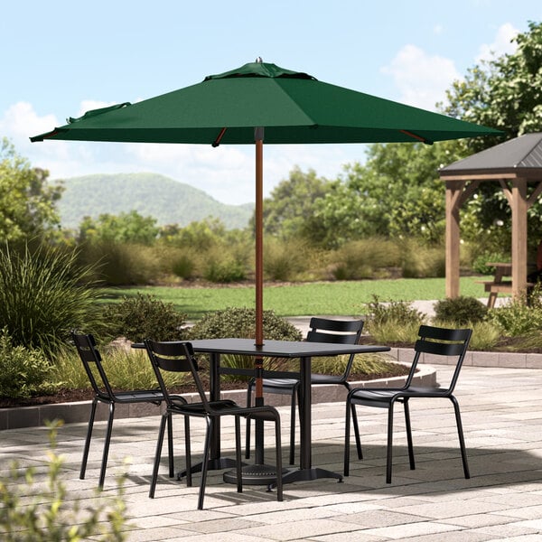 A Lancaster Table & Seating forest green umbrella on a patio table with chairs.