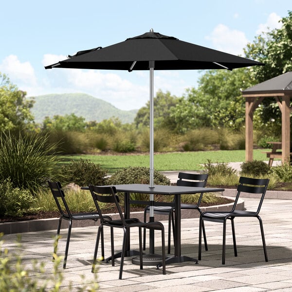 A Lancaster Table and Chairs under a black umbrella on a stone patio.