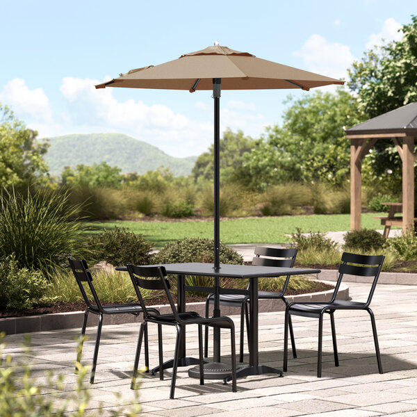 A Lancaster Table & Seating wheat table and chairs with a black umbrella on a stone patio.