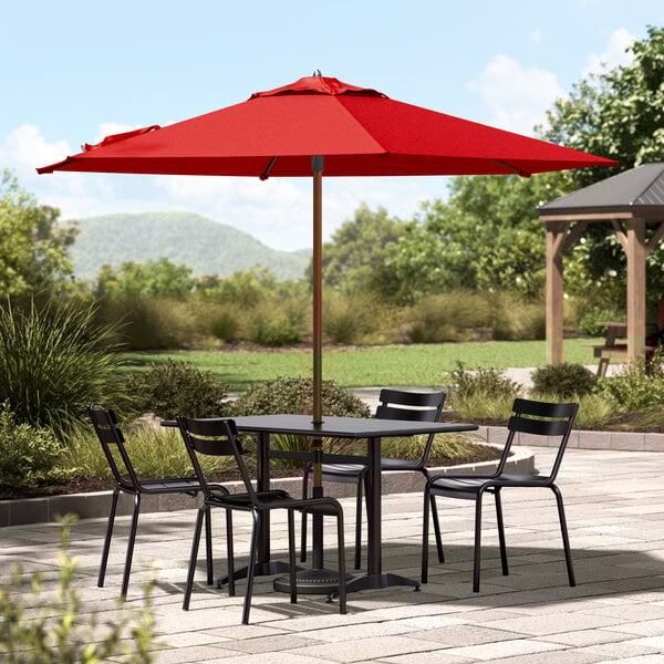 A Lancaster Table & Seating woodgrain table and chairs under a red umbrella on a patio.