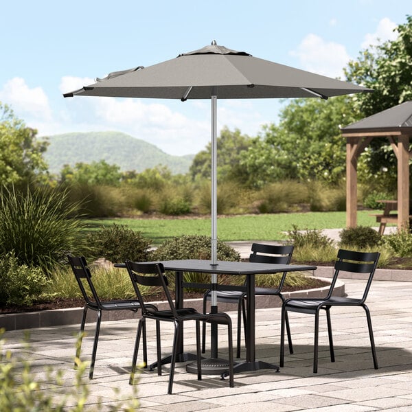 A Lancaster Table & Seating round silver aluminum umbrella on a table with chairs on a patio.