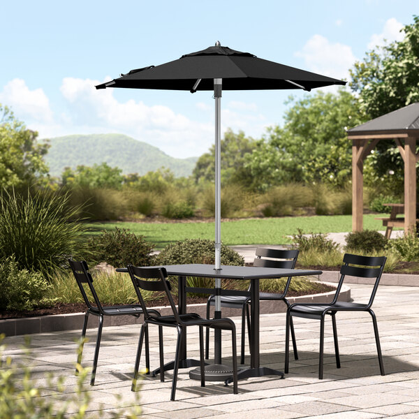 A black table and chairs under a Lancaster Table & Seating black umbrella on a stone patio.