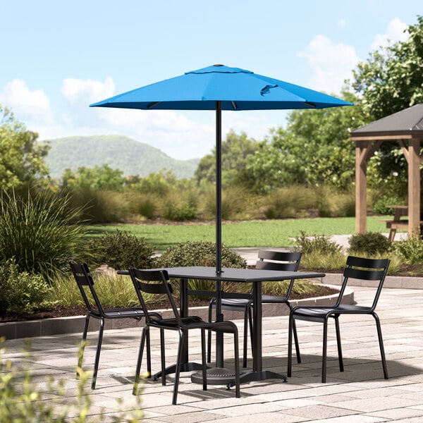 A black table and chairs under a blue Lancaster Table & Seating umbrella on a patio.