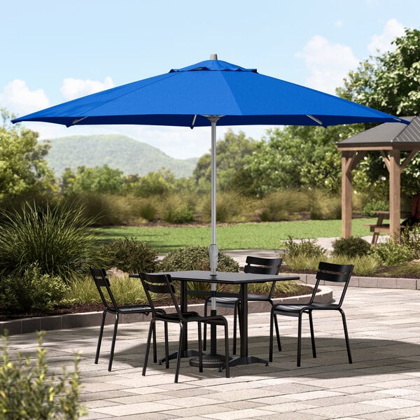 A Lancaster Table & Seating silver aluminum umbrella with a cobalt blue canopy over an outdoor patio table.